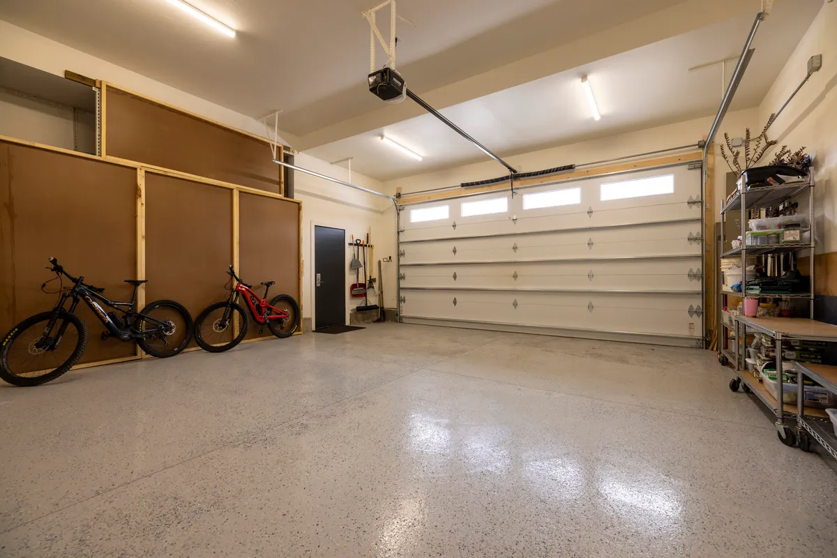 A spacious garage interior featuring two bicycles, storage shelving, and an open garage door, emphasizing ample room for gear storage and easy access for outdoor equipment and adventure prep.