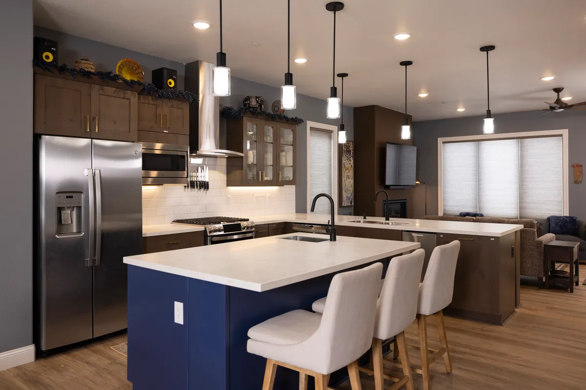 A contemporary kitchen scene with a large island countertop, sleek stainless steel appliances, pendant lighting, and bar stools. The space is lively and built for social interaction, echoing the lively atmosphere described in the section.