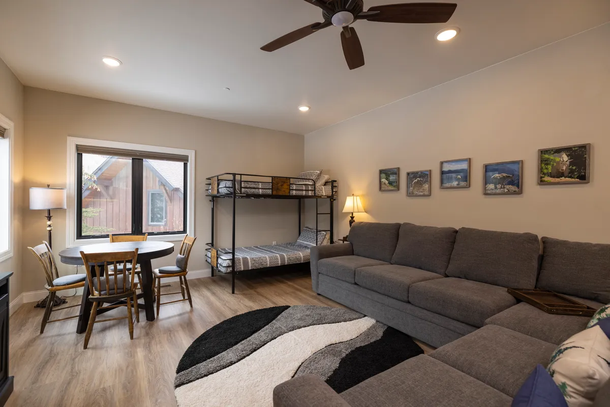 A welcoming loft space with a bunk bed, sectional sofa, and a dining/game table. Artwork on the wall and soft lighting create a cozy, playful atmosphere ideal for kids and adults alike.