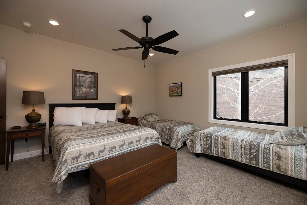 A warm, inviting bedroom with a king-sized bed and two twin beds, accented by a wooden trunk and soft ambient lighting from table lamps. The space is styled for relaxation and family comfort, offering both privacy and togetherness.