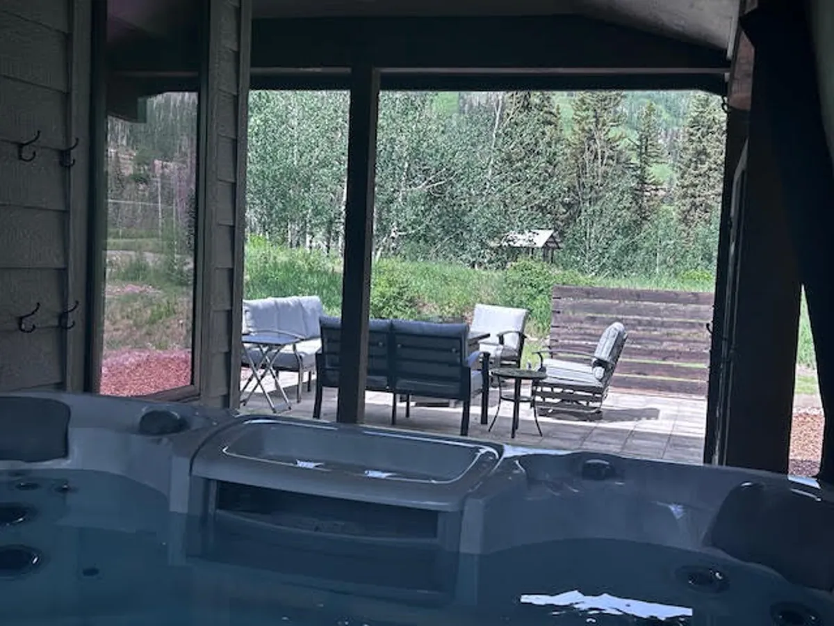 This image features a private hot tub on a sheltered patio, surrounded by outdoor seating and lush greenery. The view extends toward the natural landscape, suggesting a tranquil and exclusive setting ideal for relaxation.