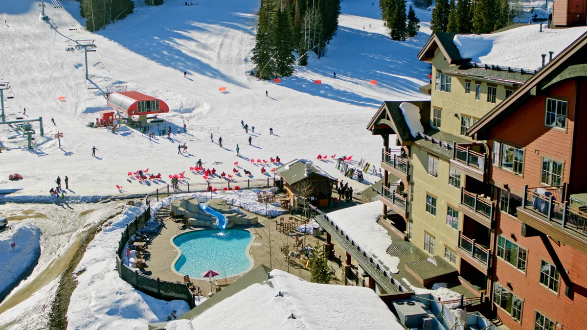 An energetic exterior scene showing snow-covered ski slopes, a swimming pool area, and the distinctive lodge architecture, with people skiing, snowboarding, and enjoying the pool. The image blends active resort life with cozy retreat elements.