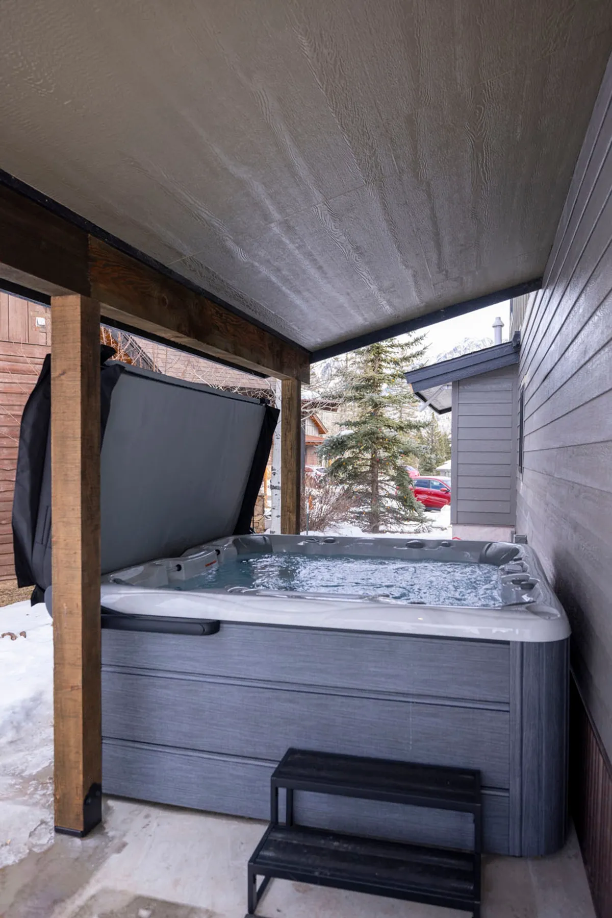 An inviting outdoor hot tub surrounded by wooden beams and a snow-covered landscape. The hot tub steams in the cold air, hinting at warmth and relaxation, while the wintry setting highlights the contrast between indoor comfort and the crisp mountain environment.